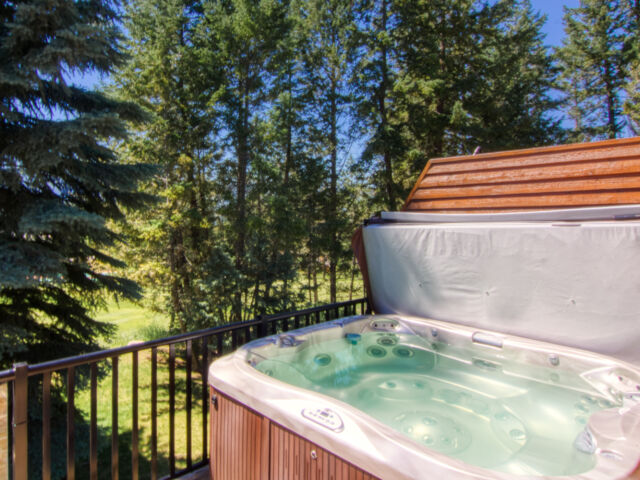 Wood paneled porch hot tub on a deck with its lid off. The water in the hot tub is clear. Porch overlooks treed area.